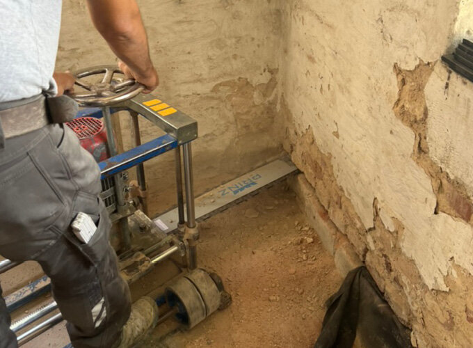 Ein Handwerker durchtrennt mit einer Mauersäge eine freigelegte Wand horizontal knapp über der Bodenplatte, um das Mauerwerk trocken zu legen.