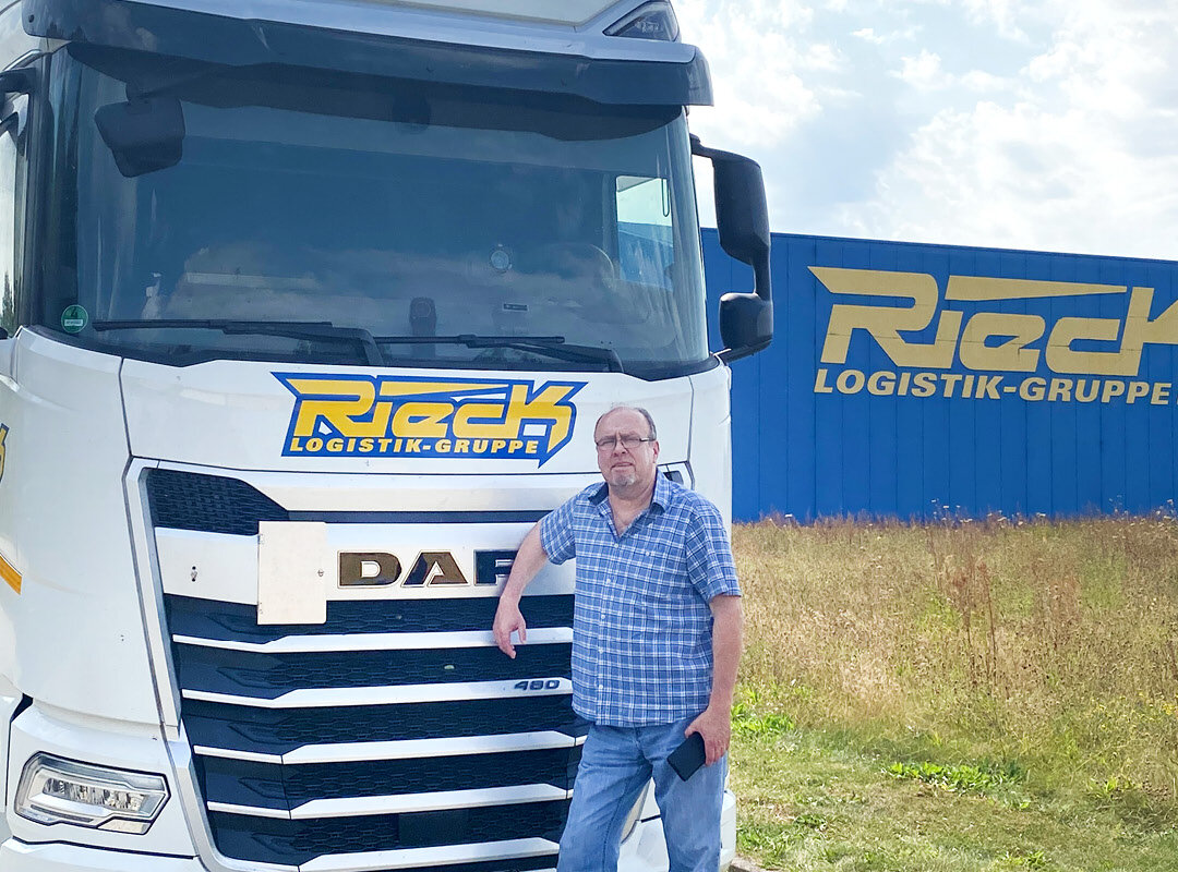 Andreas Wolff steht vor einem Kuhltransporter. Rechts ist eine Halle von Rieck zu sehen.