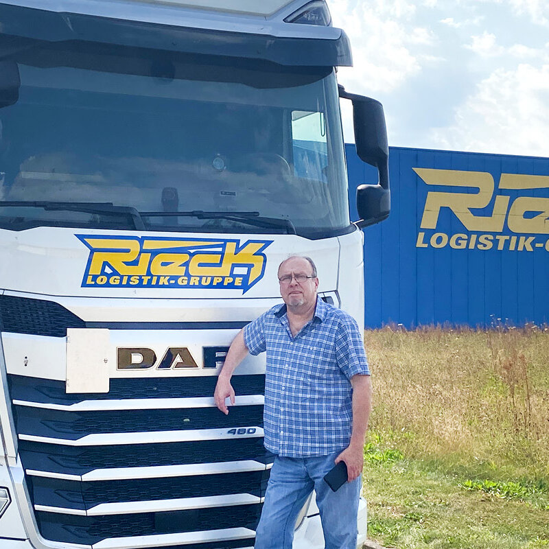 Andreas Wolff steht vor einem Kuhltransporter. Rechts ist eine Halle von Rieck zu sehen.