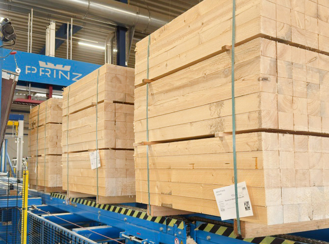 Auf dem Förderband einer großen Sägeeinheit fahren quadratisch formatierte Holzbretterpakete.