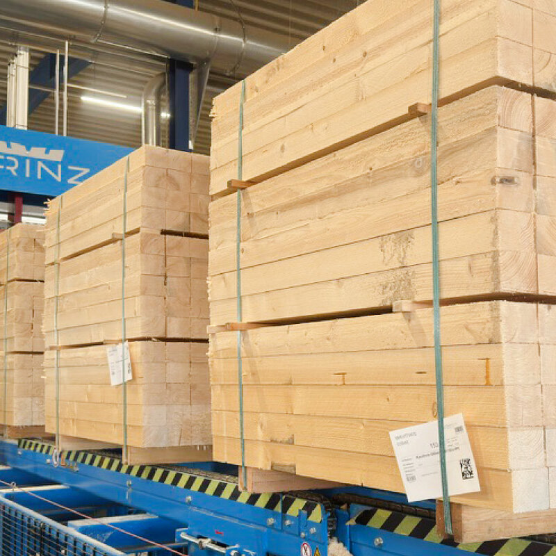 Auf dem Förderband einer großen Sägeeinheit fahren quadratisch formatierte Holzbretterpakete.