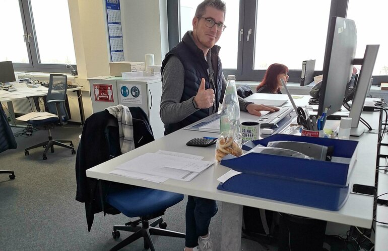 Foto: Mann in einem Büro steht an einem höhenverstellbaren Schreibtisch
